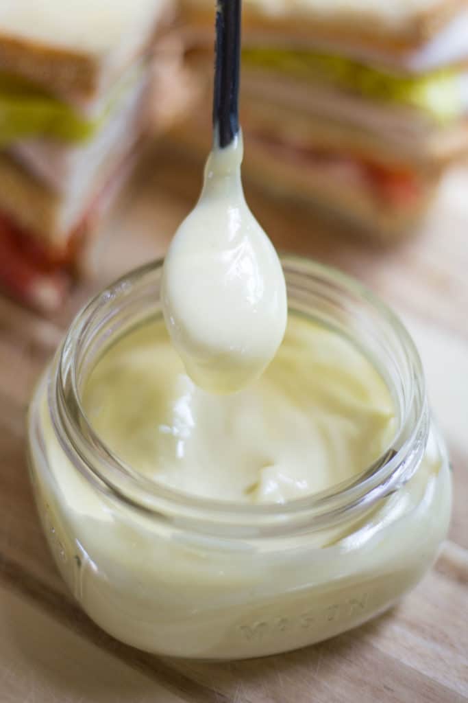A spoon dipped in a clear jar of homemade mayonnaise 