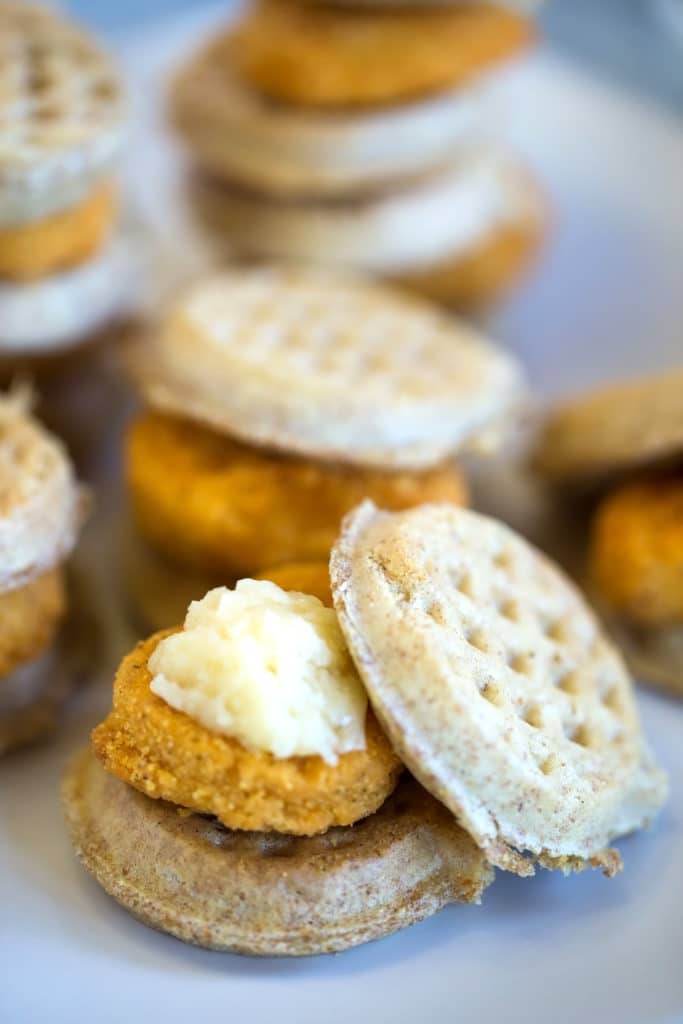 A chicken nugget topped with butter sandwiched between miniature waffles