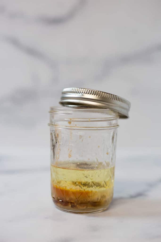 A clear mason jar filled 1/3 way up with salad dressing ingredients with the lid partially on
