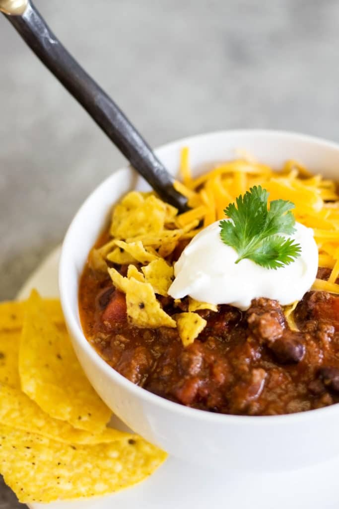 Bowl of chili garnished with cilantro, sour cream, tortilla chips, and grated cheese