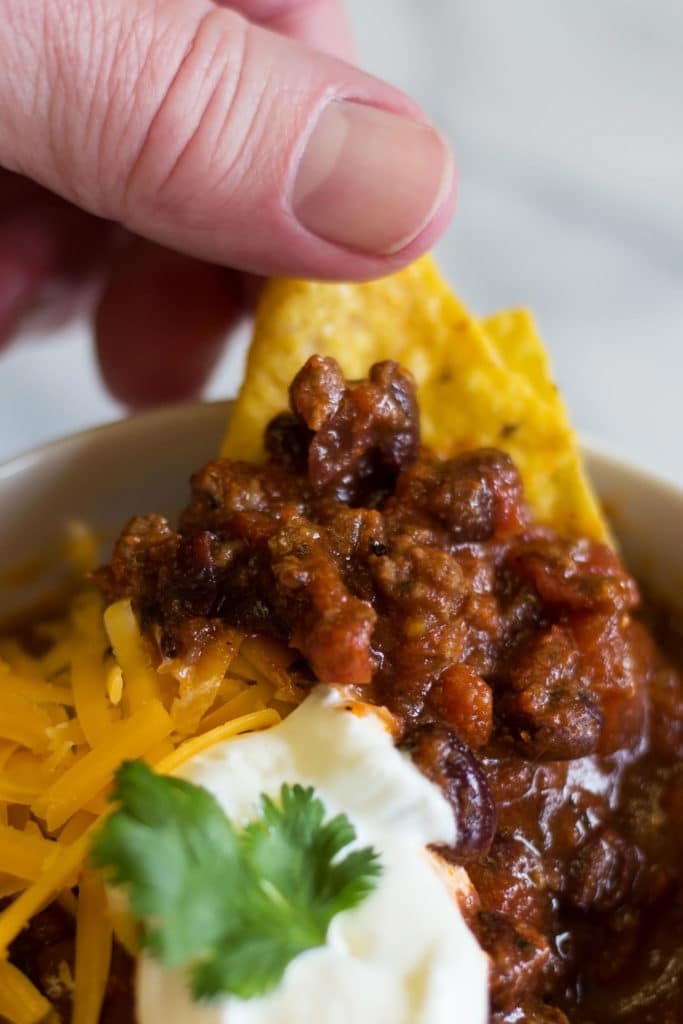 Hand scooping chili from bowl with tortilla chip
