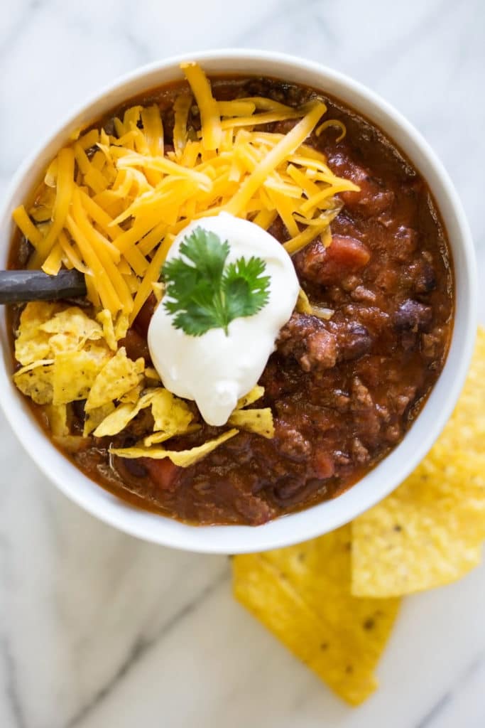 Bowl of chili garnished with cilantro, sour cream, chips, and cheese