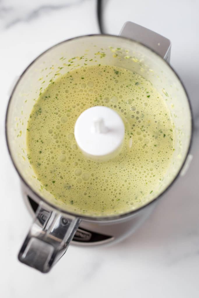Overhead view of a food processor filled with a green colored sauce