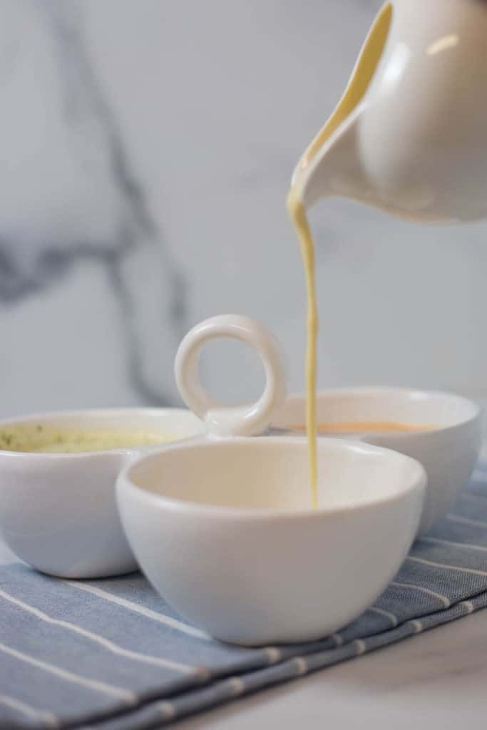 A white vessel pouring hollandaise sauce into a dish