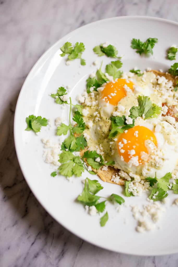 White plate with 2 sunny side up eggs garnished with cilantro, cotija cheese, and hollandaise sauce