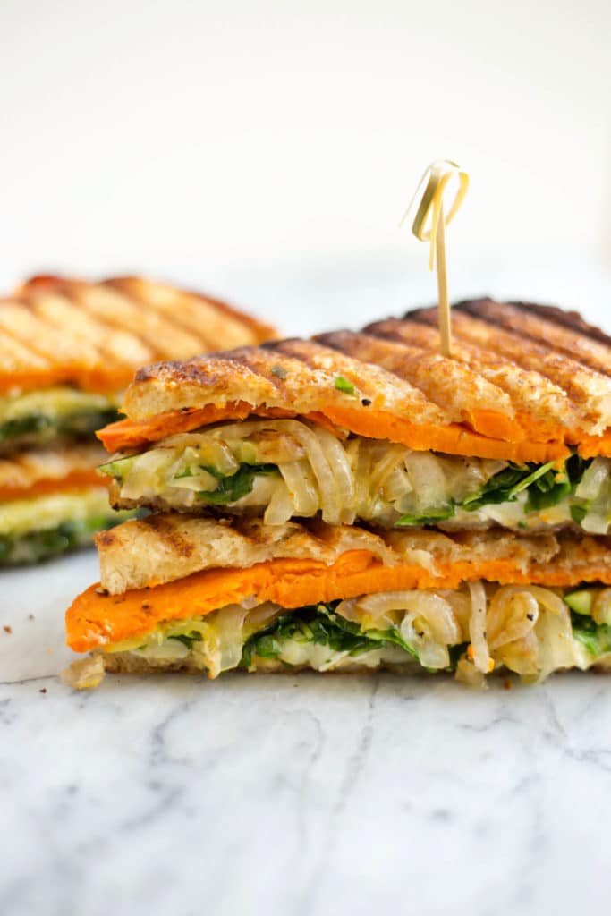 Two halves of a toasted vegetable sandwich stacked with a toothpick in the top