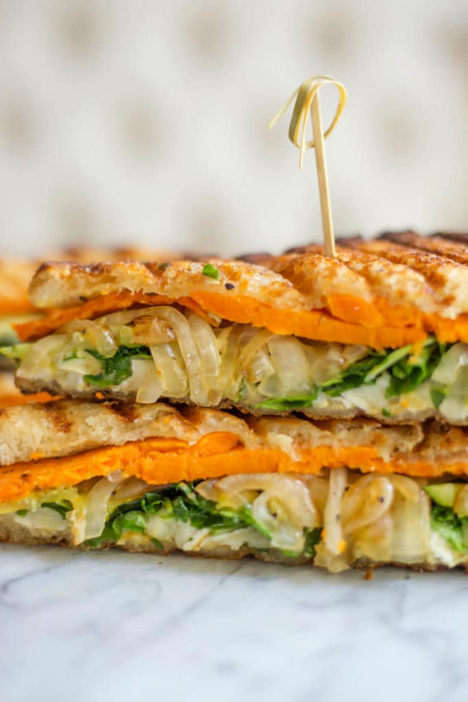 Close up of two halves of a sliced veggie and brie sandwich stacked with a toothpick in the top