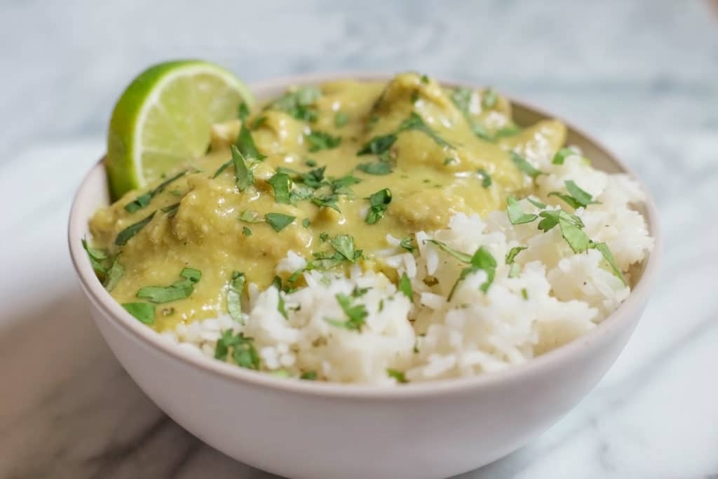 White bowl of guatemalan stew served over white rice garnished with lime and cilantro