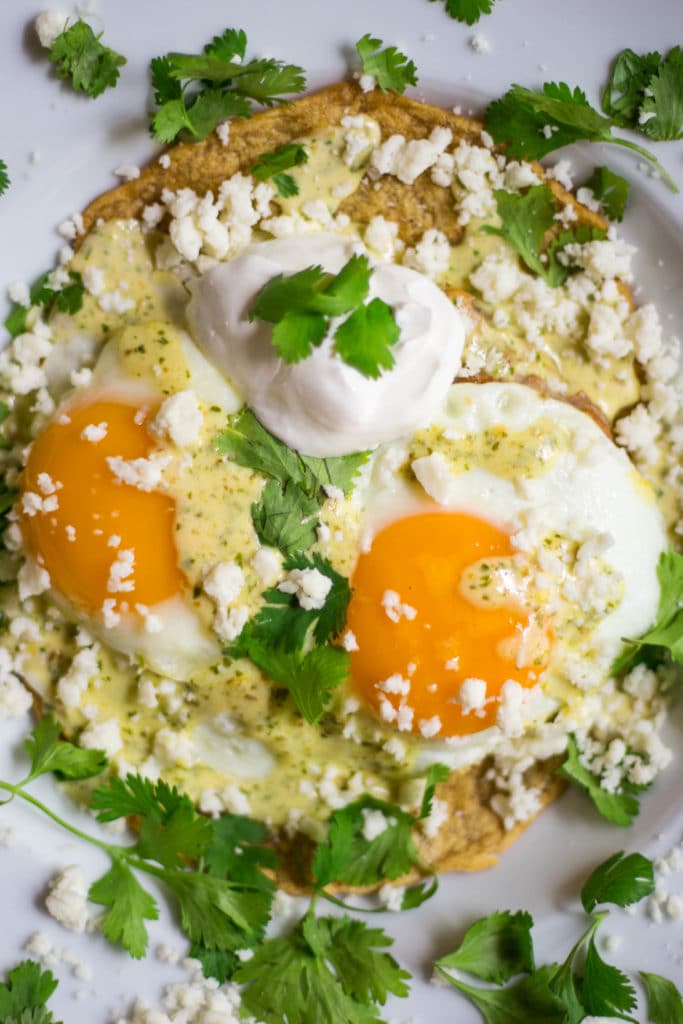 2 sunny side up eggs garnished with sour cream, hollandaise sauce, cilantro, and cotija cheese