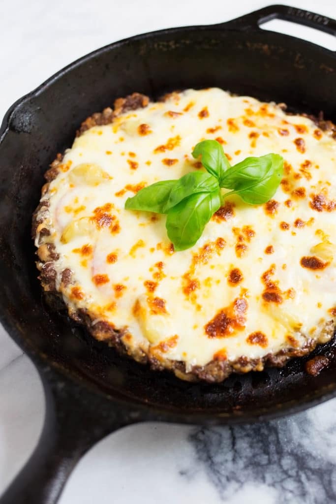 Beef crust pizza topped with melted cheese in a cast iron skillet