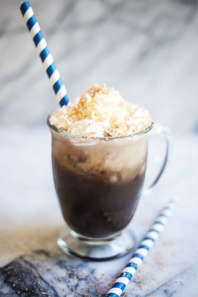 A clear coffee mug with iced coffee topped with whipped cream and a blue striped straw