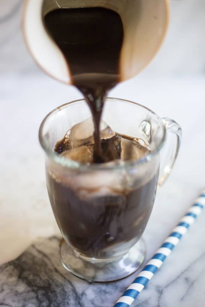 Pouring dark coffee into a clear mug filled with ice and a blue striped straw