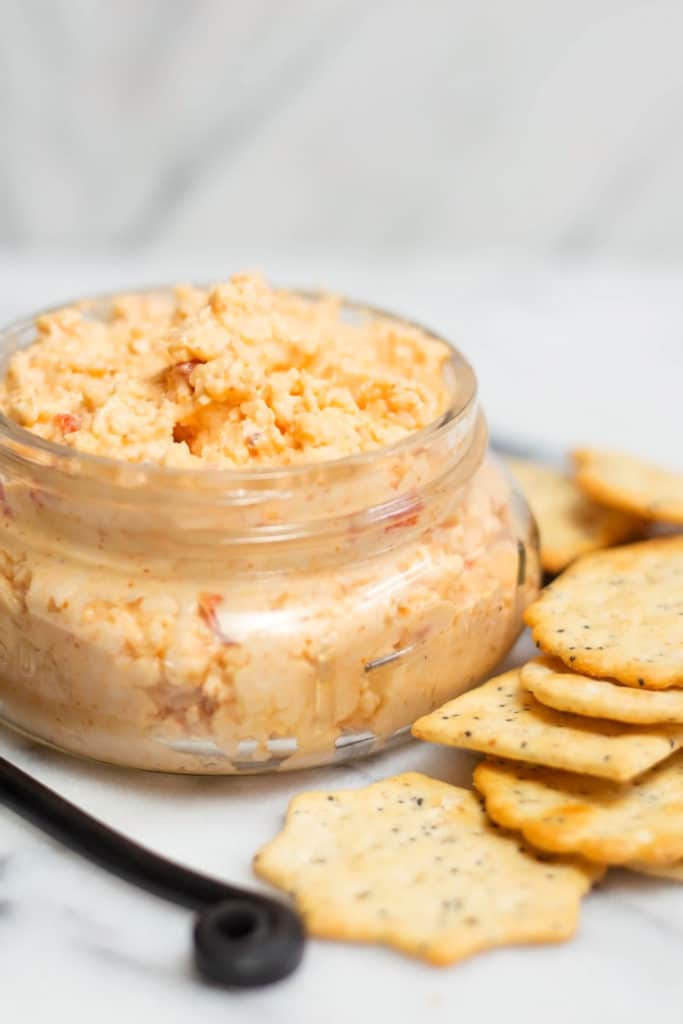 Clear jar of pimento cheese spread surrounded by crackers