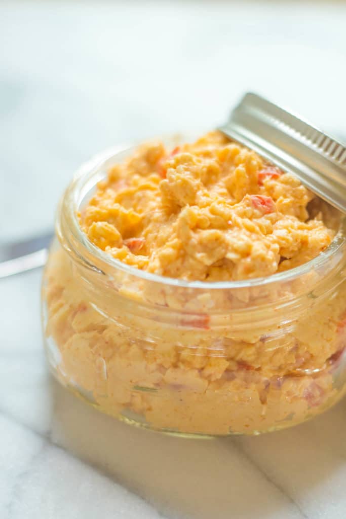 Clear jar filled with pimento cheese on a white surface with a white background
