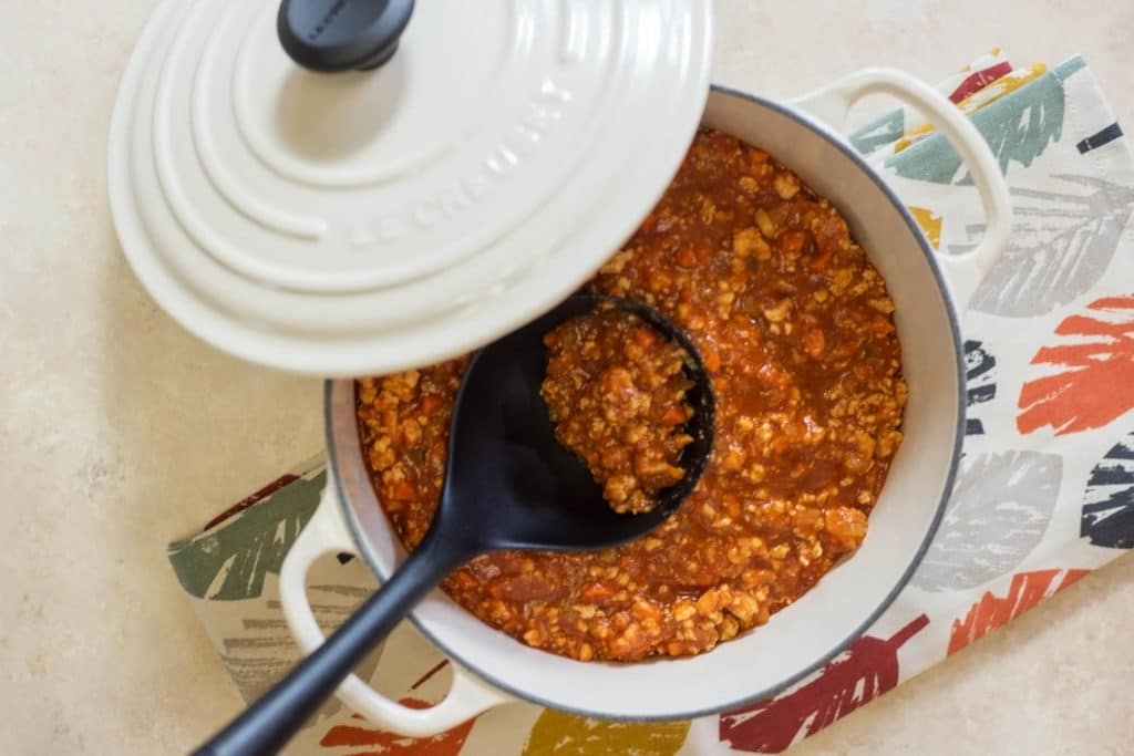 An overhead shot of a white dutch oven with a black ladle filled with buffalo chicken chili