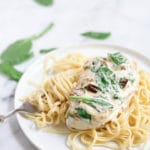 White plate of Tuscan chicken over pasta