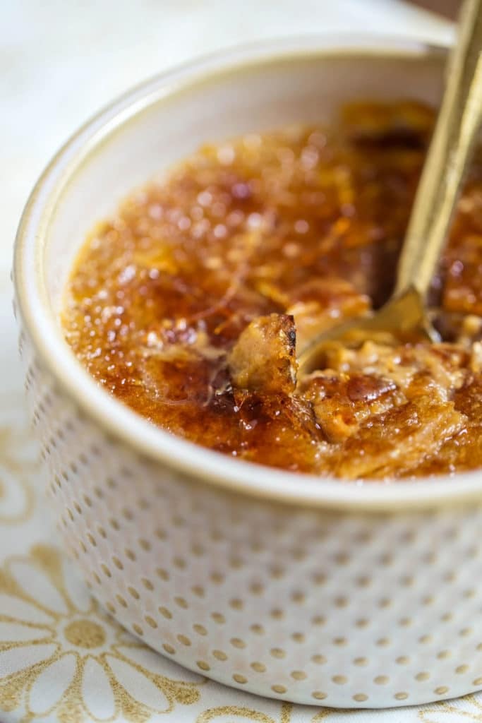 A ramekin of creme brulee with a gold spoon that has cracked the hard sugar topping