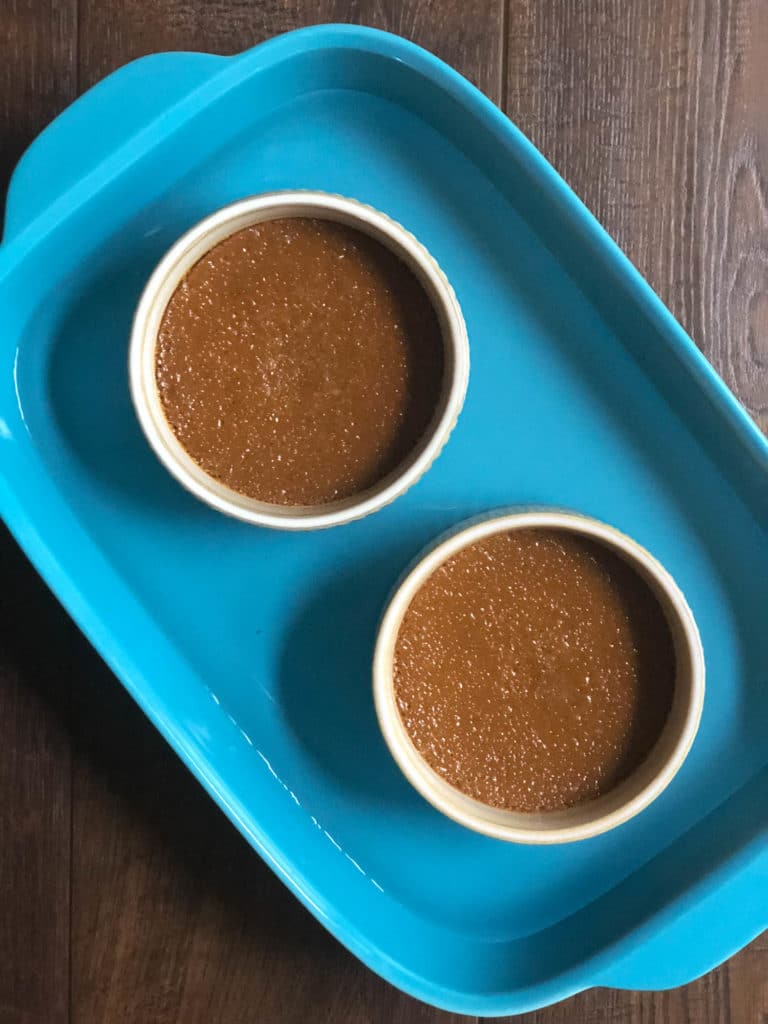 Overhead view of 2 ramekins filled with brown custard in a larger blue baking dish