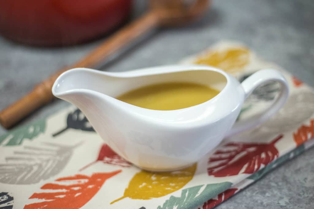 A white gravy boat filled with gravy on a fall napkin