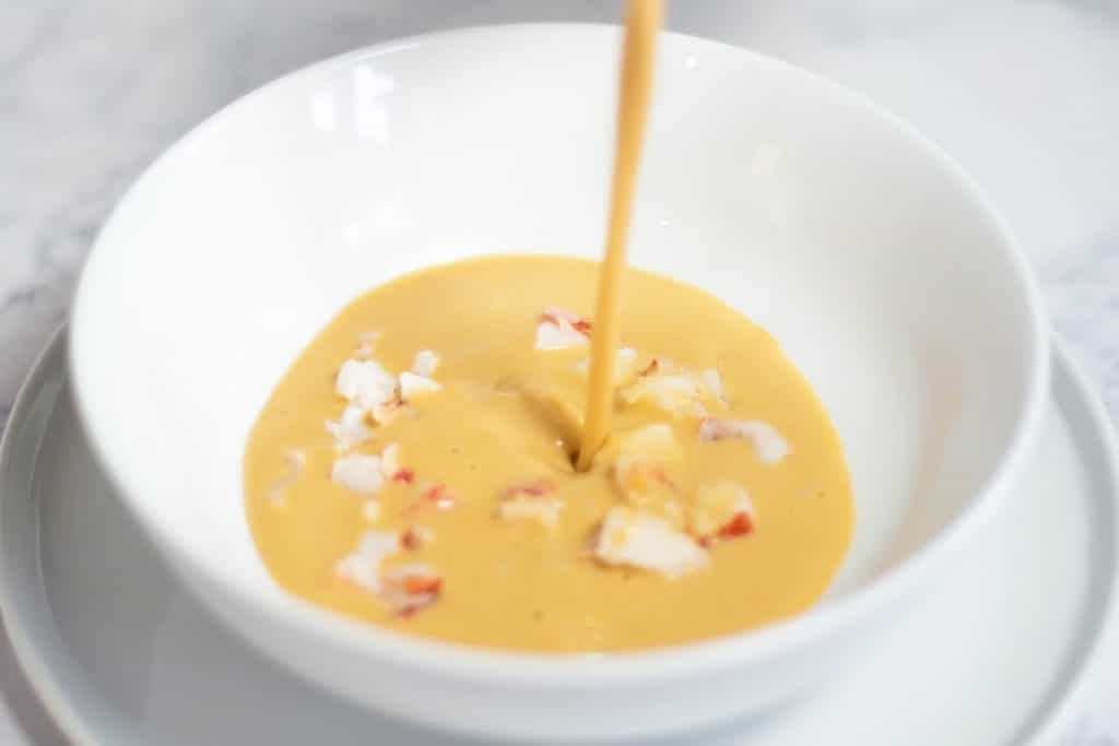 White bowl with bits of lobster and bisque being poured over the top