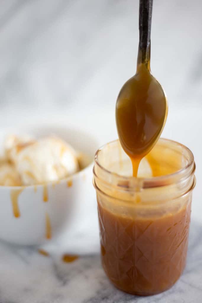 jar of caramel sauce with spoon coated with caramel sauce and bowl of ice cream topped with caramel sauce