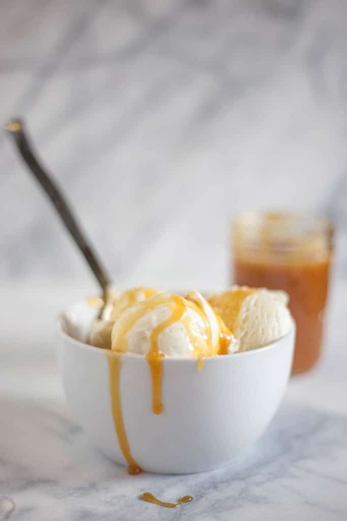 Bowl of ice cream drizzled with caramel sauce and jar of caramel sauce in background