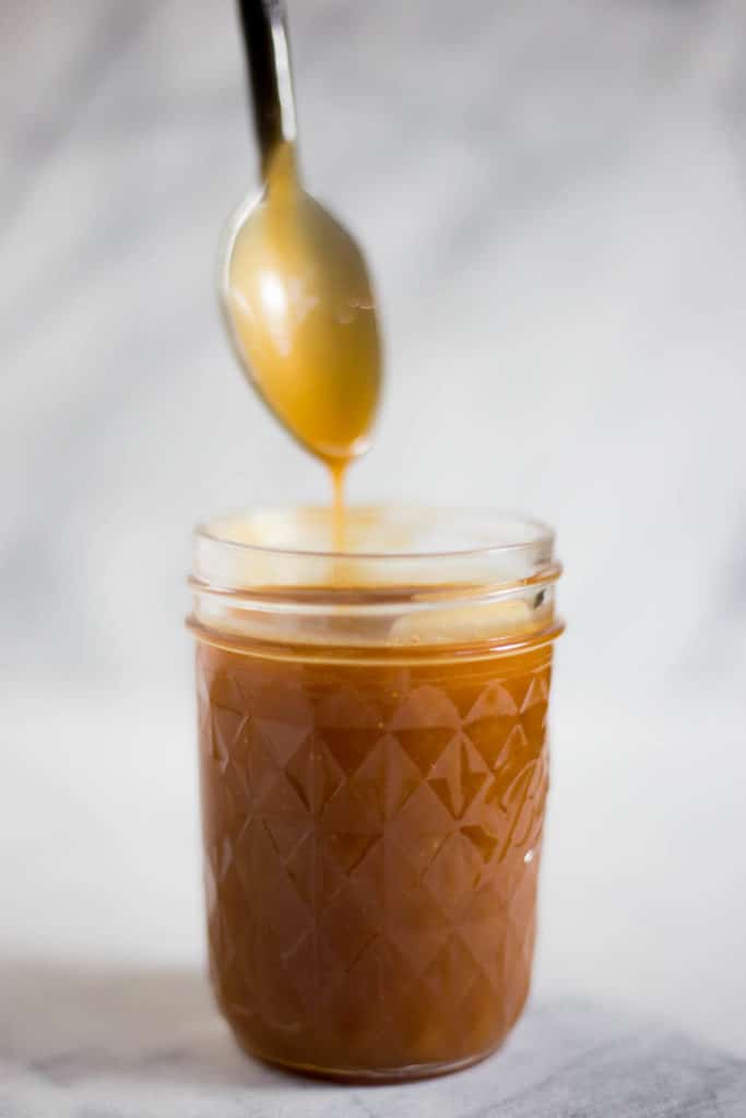 jar of caramel sauce with spoon coated with caramel sauce