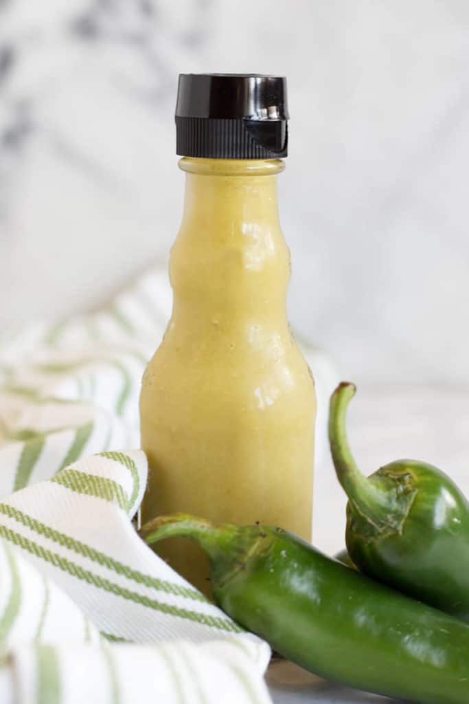 Jar of green hot sauce and 2 jalapeno peppers