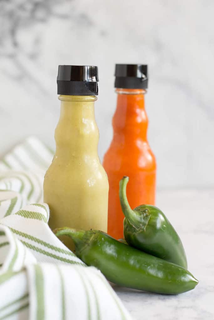 Jar of red and jar of green hot sauce with 2 jalapeno peppers