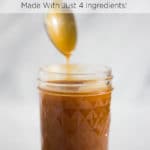 A spoon coated with caramel sauce above a clear jar of caramel sauce