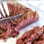 A corned beef brisket being sliced on a marble cutting board