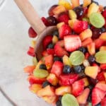 Clear bowl of fruit salad with wooden spoon