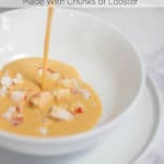 Bisque being poured into a white bowl with chunks of lobster