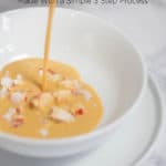 Bisque being poured over chunks of lobster in a white bowl
