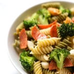 A white bowl with tri colored rotini noodles, sliced pepperoni, and broccoli florets