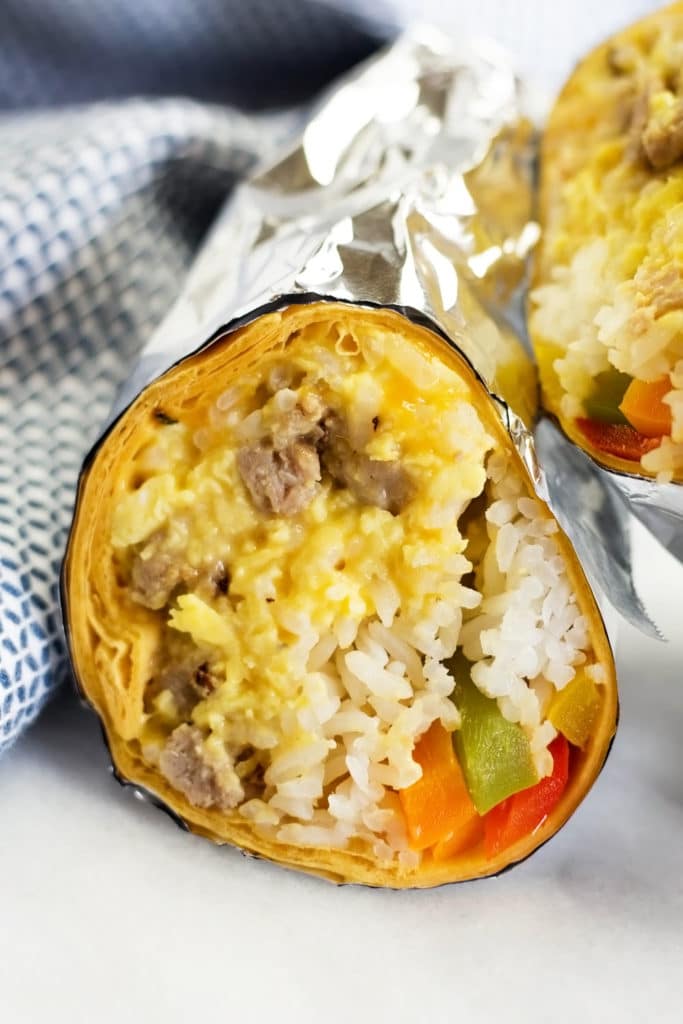 Breakfast burrito with rice, peppers, sausage, eggs and cheese wrapped in foil and cut in two