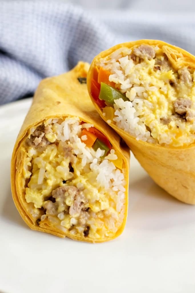 A breakfast burrito with rice, peppers, sausage, eggs, and cheese cut in two