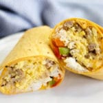 A breakfast burrito with rice, peppers, sausage, eggs, and cheese cut in two