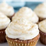 A group of carrot cake cupcakes topped with white frosting sprinkled with gold sugar