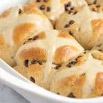 A white baking dish with baked hot cross buns made with chocolate chips