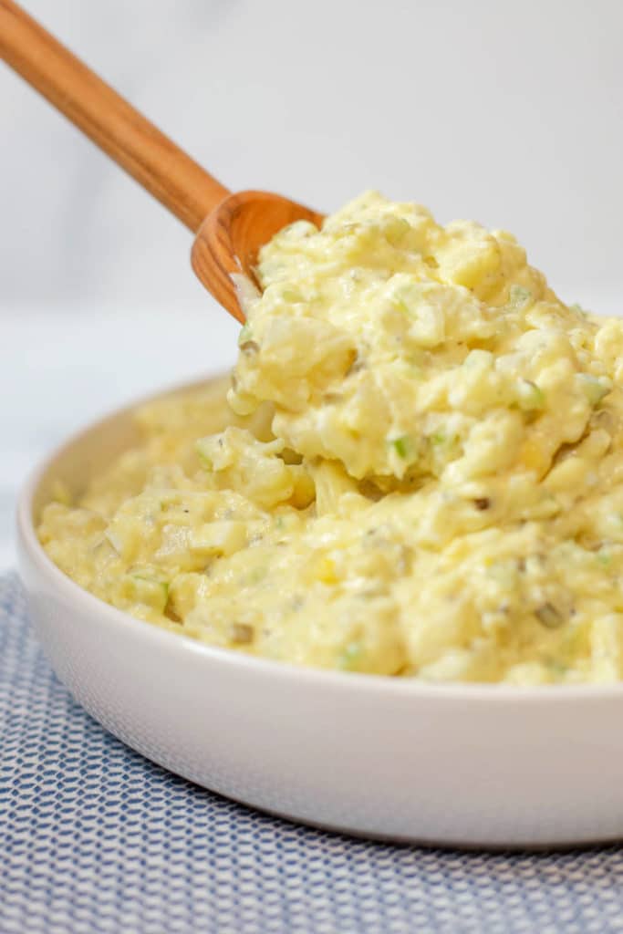 A wooden spoon scooping potato salad from a white bowl