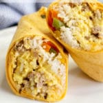 A burrito with eggs, rice, peppers, sausage, and cheese cut in half