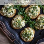 A black tray topped with small round crostini with a creamy topping garnished with chopped parsley