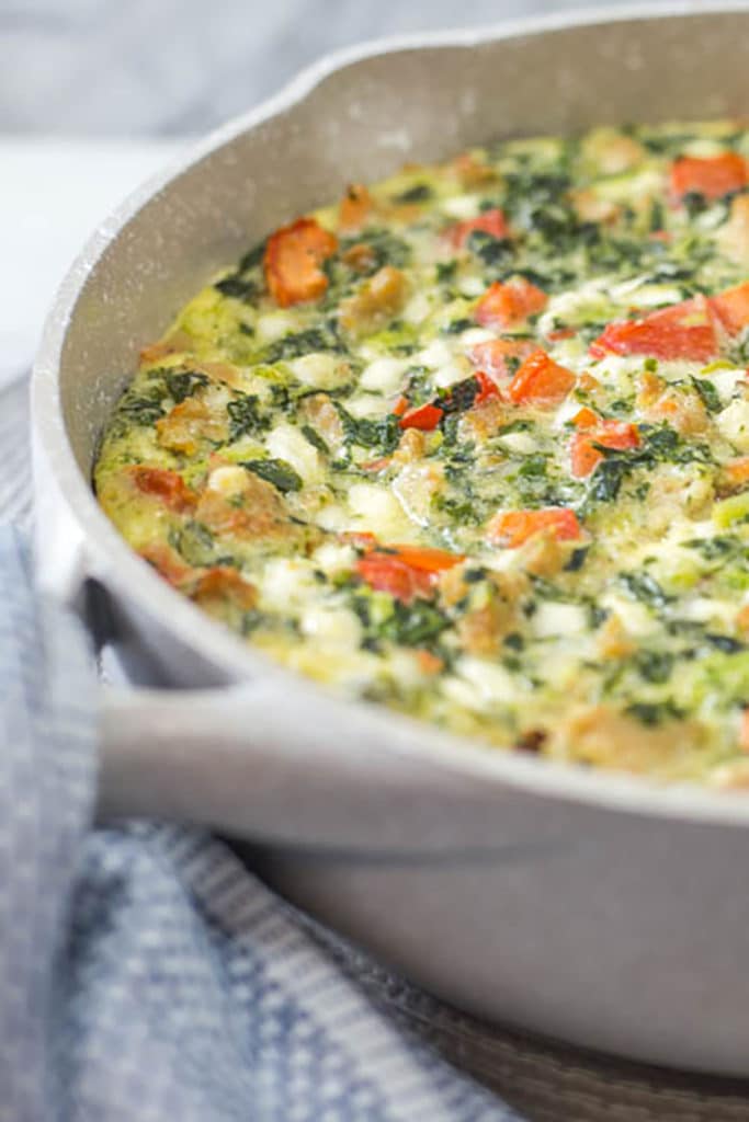 Upclose view of a tan skillet of cooked frittata with tomatoes and spinach