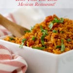 A wooden spoon inside a white bowl filled with Mexican rice next to a red striped napkin