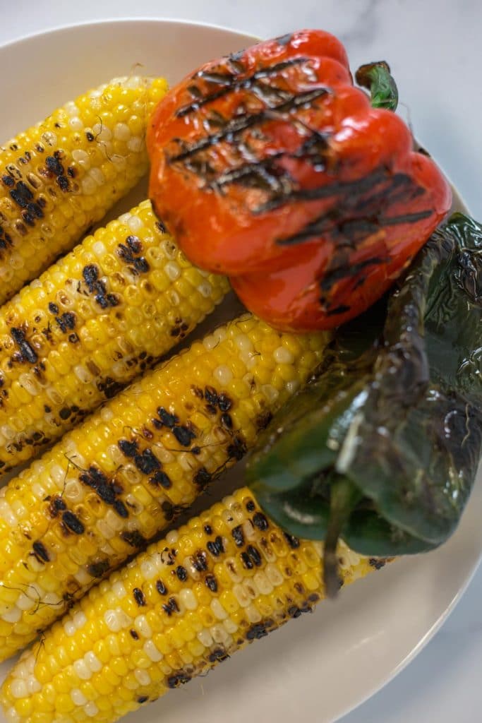 Overhead view of 4 ears of grilled corn, a charred red pepper, and a charred poblano pepper