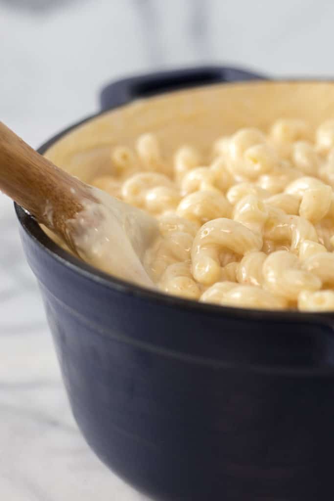 A wooden spoon dipped into a blue dutch oven filled with mac and cheese