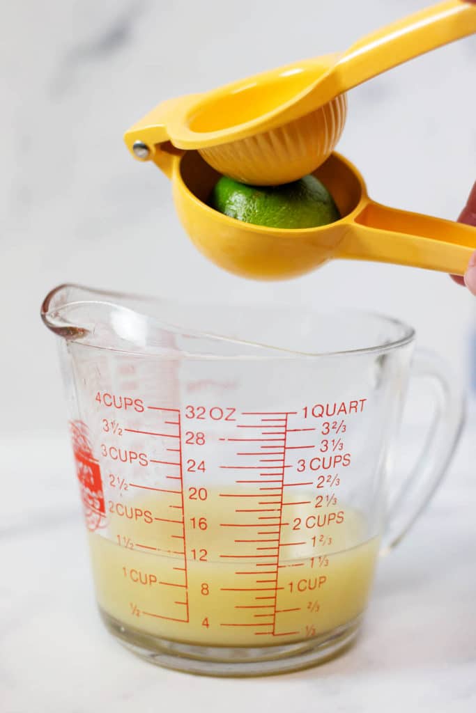 A lime in a juicer over the top of a glass measuring cup partially filled with lime juice