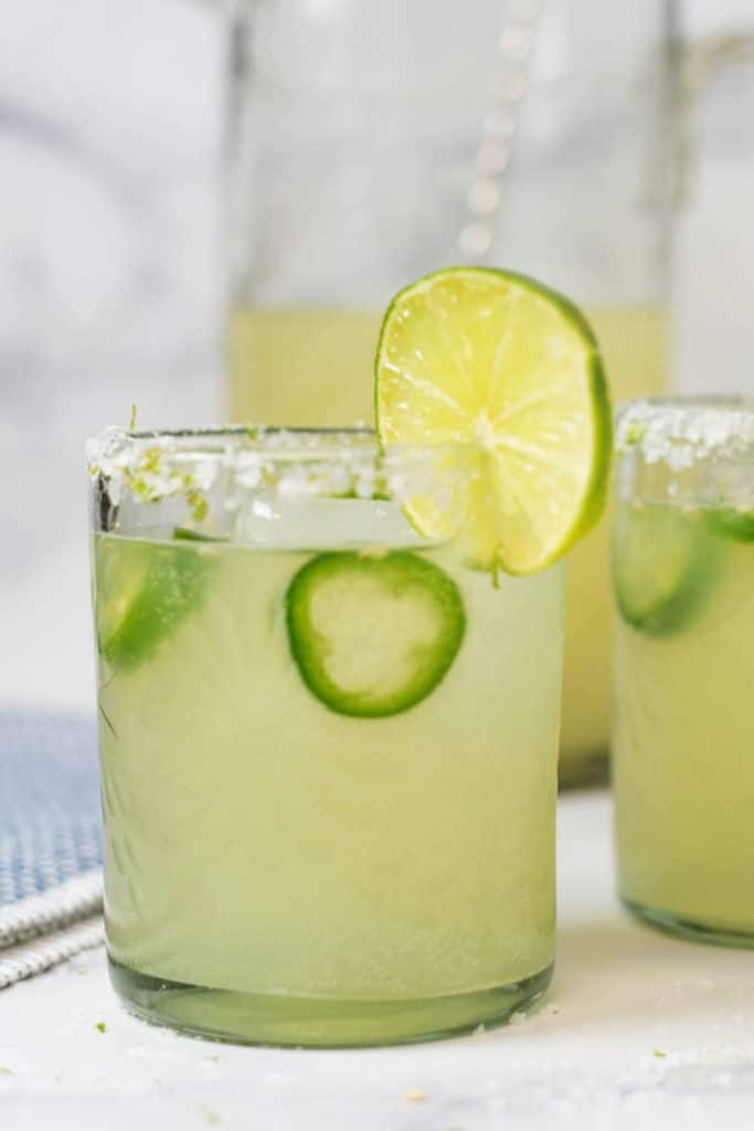 Two glasses of margaritas with slices of jalapenos and a slice of lime on the rim
