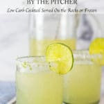 Two glasses of margaritas with slices of lime on the rim with a pitcher of margaritas in the background